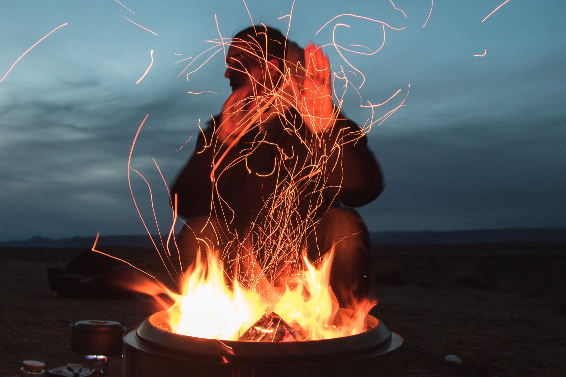 man sitting facing fire in pot during night